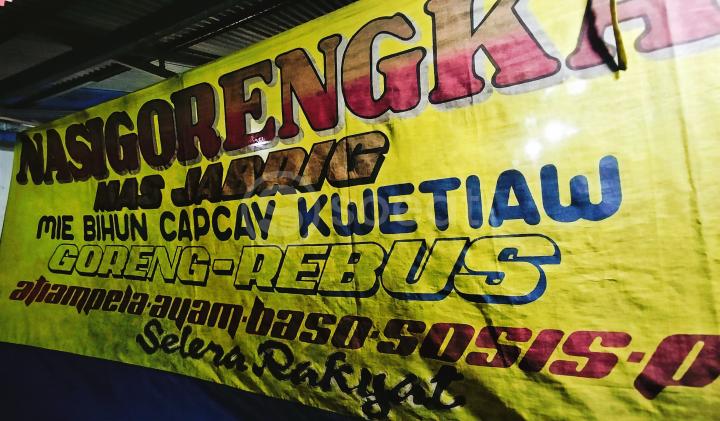 Spanduk menjadi inti seluruh ekosistem sosial-ekonomi dan budaya tenda kuliner kaki lima. 